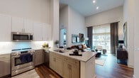 This single-floor residence is defined by its dramatic, soaring ceilings that lend an airy, expansive quality to the open-concept living and kitchen area. The kitchen is thoughtfully designed with granite countertops, a large central island with bar seating, stainless steel appliances including a French-door refrigerator, under-cabinet lighting, and a mix of white upper and warm wood-toned lower cabinetry. The island doubles as a dining and prep space, seamlessly connecting to the living area.

The living room benefits from oversized sliding glass doors that open onto a private balcony, filling the space with natural light and offering outdoor views of the surrounding community. Tall ceilings continue here, reinforcing the open, loft-like atmosphere.

Both bedrooms are carpeted and comfortably scaled, each featuring large windows with outdoor views and ample natural light. The bedrooms share access to well-designed bathrooms, each featuring granite-topped wood-toned vanities, large rectangular mirrors, light tile flooring, and direct access to walk-in closets with built-in shelving and hanging storage. Rich hardwood flooring flows through the main living areas, complementing the residence's modern, cohesive aesthetic throughout.