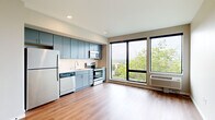 Located at 590 Park St in Saint Paul, Minnesota, this efficiently designed studio unit offers a thoughtfully organized open-concept layout that combines the living area and kitchen into one cohesive space. Warm-toned hardwood-style flooring runs throughout, creating a clean and consistent aesthetic.

The kitchen is a standout feature, equipped with sleek blue-gray cabinetry extending to the ceiling for ample storage, a white subway tile backsplash, and a full suite of stainless steel appliances including a refrigerator, electric range, over-the-range microwave, and dishwasher. A single-basin sink sits beneath recessed lighting, adding to the kitchen's functional design.

The open living area is bright and airy, anchored by large black-framed windows that invite generous natural light and frame views of the surrounding tree canopy and Saint Paul skyline. A wall-mounted HVAC unit provides in-unit climate control.

The bathroom features a clean, modern design with gray cabinetry, a wide white countertop vanity, a large mirror, and a glass-enclosed shower, all finished with the same hardwood-style flooring found throughout the unit. A utility panel is conveniently located near the entryway. The overall ambiance is modern, minimal, and move-in ready.