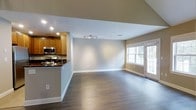 This well-appointed 2-bedroom, 2-bathroom residence is spread across two floors, offering a thoughtfully designed layout that balances comfort and functionality. The open-concept main living area features rich, dark hardwood flooring that flows seamlessly from the kitchen through to the living space, creating a cohesive and inviting atmosphere. Recessed lighting and a track light fixture illuminate the interior, complementing the abundant natural light that pours in through large windows. Neutral-toned walls provide a versatile backdrop throughout the home. The kitchen is equipped with warm wood cabinetry, stainless steel appliances including a microwave and range, and a dark-topped peninsula that doubles as a breakfast bar — ideal for casual dining or entertaining. The open living area is generously sized, offering ample room for a variety of furniture arrangements, with a bright window and glass door providing views to the outdoors. The two-floor layout offers a natural separation between living and sleeping spaces, enhancing privacy and livability. With its clean finishes, modern fixtures, and practical design, this residence presents a comfortable and move-in-ready home suitable for a wide range of lifestyles.