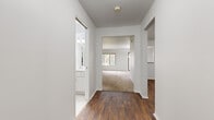 This single-floor home offers a clean, functional layout designed for comfortable everyday living. The interior is defined by a consistent design palette of crisp white walls and rich, dark hardwood-style flooring that runs through the main living and kitchen areas, creating a warm contrast throughout.

The kitchen is well-equipped with ample light wood cabinetry providing generous storage above and below the counter, a double sink, a full suite of white appliances including a dishwasher and electric range, and a built-in range hood. The kitchen opens toward the living area, enhancing the sense of connectivity between spaces.

The living and bedroom areas feature plush wall-to-wall carpeting, lending a comfortable, quiet feel underfoot. Bedrooms are naturally lit by sliding windows that frame views of lush greenery outside. A spacious walk-in closet with built-in shelving and a hanging rod offers excellent storage for the primary bedroom.

The bathroom includes a full soaking tub with white tile surround, mosaic tile flooring, and a bright vanity with a large mirror. A dedicated laundry room with a full-size washer and dryer adds practical convenience. The central hallway connects all areas of the home efficiently, giving the overall layout a cohesive, easy-to-navigate flow.