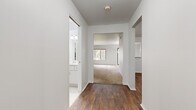 This single-floor home offers a clean, functional layout designed for comfortable everyday living. The interior is defined by a consistent design palette of crisp white walls and rich, dark hardwood-style flooring that runs through the main living and kitchen areas, creating a warm contrast throughout.

The kitchen is well-equipped with ample light wood cabinetry providing generous storage above and below the counter, a double sink, a full suite of white appliances including a dishwasher and electric range, and a built-in range hood. The kitchen opens toward the living area, enhancing the sense of connectivity between spaces.

The living and bedroom areas feature plush wall-to-wall carpeting, lending a comfortable, quiet feel underfoot. Bedrooms are naturally lit by sliding windows that frame views of lush greenery outside. A spacious walk-in closet with built-in shelving and a hanging rod offers excellent storage for the primary bedroom.

The bathroom includes a full soaking tub with white tile surround, mosaic tile flooring, and a bright vanity with a large mirror. A dedicated laundry room with a full-size washer and dryer adds practical convenience. The central hallway connects all areas of the home efficiently, giving the overall layout a cohesive, easy-to-navigate flow.