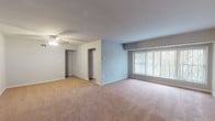 This single-floor unit offers a thoughtfully organized layout across a generous footprint. The expansive main living area is finished with warm neutral carpeting and painted in soft, light gray tones, creating a clean and inviting atmosphere. A ceiling fan overhead and a large picture window with vertical blinds allow natural light to fill the room while providing views of the surrounding greenery. The open layout connects seamlessly to additional living or dining space, also carpeted and ceiling fan-equipped, offering flexibility in use.

The kitchen features light wood cabinetry, dark stone-look countertops, tile flooring, and black appliances including a gas range with overhead exhaust and a dishwasher, complemented by a stainless steel sink — a practical and efficient cooking space.

The bedrooms are generously sized, each with soft carpeting, neutral gray walls, and windows that bring in natural daylight. One bedroom includes direct access to a full bathroom, complete with a tiled tub-shower surround, a white vanity, and classic fixtures. A second bathroom serves as a half-bath with a vanity, mirror with overhead lighting, and tile flooring.

Throughout the unit, clean white trim, consistent neutral tones, and a practical design create a comfortable and move-in-ready living environment.