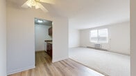 Located at 6871 Ames Rd in Parma, OH, this single-floor unit offers a functional and straightforward layout across two bedrooms, one bathroom, and a collection of well-defined living spaces. The living room is generously proportioned, featuring soft wall-to-wall carpeting and a large window fitted with a wall-mounted air conditioning unit that fills the room with natural light. The entryway transitions seamlessly from hardwood-style flooring into the carpeted living area, creating a clear delineation between spaces. A ceiling fan adds to the room's comfort. The kitchen is efficiently designed with rich cherry wood cabinetry, granite-style countertops, under-cabinet lighting, a double-basin sink, and white appliances including a range and dishwasher, all set on light hardwood-style flooring. The bedrooms are carpeted and bright, each offering window views and wall-unit climate control. The primary bedroom includes access to a dedicated closet outfitted with wire shelving on both sides, providing ample storage. The bathroom is clean and functional, featuring a sliding-door shower stall, a cherry wood vanity with a mirrored medicine cabinet, and hardwood-style flooring. A hallway connects all rooms, contributing to the unit's cohesive and easy-to-navigate flow.