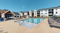 Located at 4890 Edwards Farm Rd. in Hilliard, Ohio, this residential community presents a contemporary architectural aesthetic characterized by a crisp white and neutral exterior, complemented by dark-trimmed balconies and pitched rooflines that lend the property a polished, upscale character. The building rises across multiple stories, offering residents elevated views and private outdoor balcony spaces that extend the living area into the open air.

At the heart of the community's outdoor amenities is a generously sized resort-style swimming pool, finished with clear blue water and surrounded by an expansive concrete sundeck. The deck is well-appointed with lounge chairs designed for relaxation, and shaded umbrella stations provide comfortable relief on sunny days. A covered pavilion or pergola structure is also visible, offering an additional gathering space adjacent to the pool area. The outdoor space is enclosed by clean fencing that defines the amenity zone while maintaining an open and airy feel.

The overall ambiance of the property reflects a modern residential community designed with both aesthetics and lifestyle in mind. Its location in Hilliard, Ohio, provides residents access to a suburban setting while benefiting from proximity to the greater Columbus area. The combination of thoughtful architectural design and well-developed outdoor amenities makes this a distinctive and comfortable community.