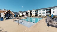 Located at 4890 Edwards Farm Rd. in Hilliard, Ohio, this residential community presents a contemporary architectural aesthetic characterized by a crisp white and neutral exterior, complemented by dark-trimmed balconies and pitched rooflines that lend the property a polished, upscale character. The building rises across multiple stories, offering residents elevated views and private outdoor balcony spaces that extend the living area into the open air.

At the heart of the community's outdoor amenities is a generously sized resort-style swimming pool, finished with clear blue water and surrounded by an expansive concrete sundeck. The deck is well-appointed with lounge chairs designed for relaxation, and shaded umbrella stations provide comfortable relief on sunny days. A covered pavilion or pergola structure is also visible, offering an additional gathering space adjacent to the pool area. The outdoor space is enclosed by clean fencing that defines the amenity zone while maintaining an open and airy feel.

The overall ambiance of the property reflects a modern residential community designed with both aesthetics and lifestyle in mind. Its location in Hilliard, Ohio, provides residents access to a suburban setting while benefiting from proximity to the greater Columbus area. The combination of thoughtful architectural design and well-developed outdoor amenities makes this a distinctive and comfortable community.