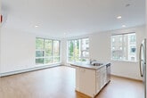 This thoughtfully designed 2-bedroom, 2-bathroom single-floor residence offers a clean, modern aesthetic throughout. Light hardwood flooring flows seamlessly across every room, complementing the crisp white walls and creating a bright, cohesive feel.

The open-concept living, dining, and kitchen area serves as the heart of the home. The kitchen is equipped with stainless steel appliances — including a range, microwave, and refrigerator — white shaker-style cabinetry, and a central island with a stone-look countertop and built-in sink. Large, multi-pane windows flood the living and dining area with abundant natural light while offering views of the surrounding neighborhood and greenery.

The two bedrooms are comfortably sized, with the primary bedroom featuring a wall-mounted split HVAC unit for personalized climate control, supplemented by baseboard heating found throughout the unit. Three closets provide generous storage options. A dedicated laundry area and a welcoming entrance hallway with recessed lighting and ample closet access add functional convenience.

Both bathrooms are finished in a clean, minimal style with white vanities and shower/tub combinations. The overall ambiance of the residence is modern and light-filled, with a neutral palette that offers a versatile canvas for any style.