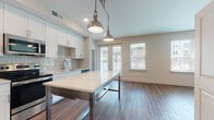 This well-appointed single-floor residence offers a thoughtfully designed layout that balances modern aesthetics with practical living. The open-concept kitchen is a standout feature, showcasing crisp white shaker cabinetry, a classic subway tile backsplash, and a full suite of stainless steel appliances including a refrigerator, range, microwave, and dishwasher. A large kitchen island with a clean white countertop and industrial-style metal base anchors the space, while two brushed nickel pendant lights hang overhead, adding a refined industrial touch. Rich wood-look flooring runs throughout the main living and kitchen areas, complementing the neutral wall tones and creating a warm, cohesive atmosphere. French doors lead to an outdoor balcony, filling the living area with natural light. The bedrooms are carpeted for comfort and each feature ceiling fans and windows with slatted blinds. Two full bathrooms are finished to a high standard — one features a double vanity with framed mirrors and brushed nickel fixtures, while the other includes a soaking tub with elegant marble-style tile surround. Walk-in closets equipped with wire shelving systems provide ample storage in multiple rooms, rounding out this move-in-ready space.