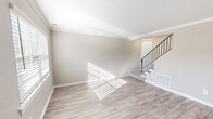Located at 1880 Village Rd in Virginia Beach, VA, this two-story, 2-bedroom, 2-bathroom home offers a thoughtfully designed layout evenly split across two floors. The main level features a bright, open living room with light-toned hardwood-style flooring, crown molding, and a stylish staircase with black iron railings. The combined kitchen and dining area is a standout, showcasing white shaker-style cabinetry, light stone countertops, a black matte faucet, and a full suite of black appliances including a refrigerator, range, over-the-range microwave, and dishwasher. Natural light filters in through plantation-shuttered windows throughout the main floor. Upstairs, both bedrooms are carpeted and equipped with ceiling fans. The generously sized primary bedroom includes a closet and ample room to furnish comfortably. The second bedroom also features a window with natural light and a ceiling fan. Six closets throughout the home provide excellent storage. Both bathrooms are finished with wood-style flooring, white vanities with black hardware, and a tub-shower combo. A dedicated laundry area adds everyday convenience. The home's neutral color palette and clean finishes create a bright, move-in-ready atmosphere.