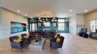 This thoughtfully designed single-floor amenity space blends modern aesthetics with functional versatility. The central lounge serves as the heart of the space, showcasing a striking teal accent wall lined with built-in shelving, a wall-mounted TV, and a fireplace. A circular tray ceiling with a sculptural sputnik chandelier adds architectural drama, while light wood-tone flooring and plush velvet seating in deep navy, accented by mustard yellow throw pillows, create an inviting, curated atmosphere. Large windows allow natural light to fill the room, and French doors provide access to the outdoors. An adjacent seating area features rich brown leather sofas, a long communal dining table, and a dramatic teal textured wall installation beneath recessed pendant lighting. The fully equipped kitchen impresses with wood-grain cabinetry, black matte countertops, open metal-framed shelving, stainless steel appliances, and a bold geometric tile floor. A game and dining area nearby continues the design story with curated artwork and mixed flooring. The fitness center offers high ceilings, full-length mirrors, a comprehensive range of equipment including free weights, resistance machines, and TRX systems. Private meeting rooms with glass-panel doors, teal walls, statement chandeliers, and stacked stone accents complete the space.