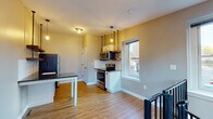 This two-floor space offers a thoughtfully designed layout that combines modern updates with industrial-inspired touches throughout. The kitchen is a standout feature, outfitted with stainless steel appliances including a refrigerator, electric range, and microwave, complemented by dark granite countertops, white cabinetry, a subway tile backsplash, and open wood shelving. Warm hardwood-style flooring runs throughout the kitchen and dining area, while pendant lighting with Edison-style bulbs adds an inviting ambiance. Natural light enters through a window overlooking the surroundings, enhancing the brightness of the space. A distinctive black metal spiral staircase serves as both a functional and architectural focal point, connecting the two floors with visual flair. The living areas feature plush carpeting and are painted in soft, neutral tones. One room showcases an exposed industrial duct running along the ceiling, contributing to the space's urban character, alongside a louvered closet door for storage. The bathroom is well-appointed with a corner neo-angle shower enclosure with dark framing, a vanity with a white countertop, and hardwood-style flooring, providing a clean and functional finish to the unit.