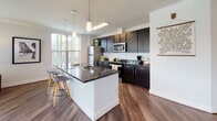 Located at 2150 Bond St. in Charlottesville, Virginia, this thoughtfully designed single-floor residence offers a cohesive blend of modern finishes and comfortable living. Rich hardwood-style flooring flows throughout the main areas, complemented by crown molding and a neutral color palette that creates a bright, welcoming atmosphere.

The entry hallway leads naturally into the heart of the home, where an open-concept kitchen and living area take center stage. The kitchen is outfitted with dark cabinetry, granite countertops, stainless steel appliances, pendant lighting, and a large central island with bar seating — ideal for both cooking and casual dining. Adjacent to the kitchen, a dining area features a sliding glass door with vertical blinds that fills the space with natural light.

The living room is generously proportioned, with expansive windows wrapping around the corner and a ceiling fan overhead, providing an airy, light-filled environment with outdoor views of the surrounding neighborhood.

The bedrooms are carpeted for comfort, each featuring large windows that allow ample daylight and views outside. Both bathrooms are finished consistently with dark vanity cabinetry, granite countertops, and hardwood-style flooring. The overall layout is efficient and well-organized, making excellent use of its single-floor footprint.