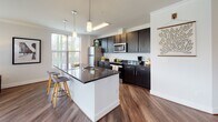 Located at 2150 Bond St. in Charlottesville, Virginia, this thoughtfully designed single-floor residence offers a cohesive blend of modern finishes and comfortable living. Rich hardwood-style flooring flows throughout the main areas, complemented by crown molding and a neutral color palette that creates a bright, welcoming atmosphere.

The entry hallway leads naturally into the heart of the home, where an open-concept kitchen and living area take center stage. The kitchen is outfitted with dark cabinetry, granite countertops, stainless steel appliances, pendant lighting, and a large central island with bar seating — ideal for both cooking and casual dining. Adjacent to the kitchen, a dining area features a sliding glass door with vertical blinds that fills the space with natural light.

The living room is generously proportioned, with expansive windows wrapping around the corner and a ceiling fan overhead, providing an airy, light-filled environment with outdoor views of the surrounding neighborhood.

The bedrooms are carpeted for comfort, each featuring large windows that allow ample daylight and views outside. Both bathrooms are finished consistently with dark vanity cabinetry, granite countertops, and hardwood-style flooring. The overall layout is efficient and well-organized, making excellent use of its single-floor footprint.