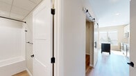 This efficiently designed one-bedroom, one-bathroom residence makes excellent use of its single-floor layout, offering a thoughtfully arranged combination of rooms finished with contemporary materials throughout. Light hardwood-style flooring flows consistently across the space, lending warmth and visual continuity from room to room.

The kitchen is a standout feature, boasting a two-tone cabinet design with crisp white upper cabinets and dark lower cabinets, complemented by a clean white countertop and stainless steel appliances including a range and microwave. A central island provides additional prep and storage space. A large window floods the kitchen with abundant natural light and offers pleasant views of the surrounding neighborhood.

The living area is bright and open, anchored by a pair of large windows that frame tree-lined rooftop views, creating an airy and inviting atmosphere. A hallway with stylish white sliding barn doors fitted with matte black hardware connects the main living areas to the private spaces, adding a modern farmhouse design element.

The bedroom is a cozy, neutral-toned retreat with clean walls and the same warm flooring found throughout. The bathroom features a dark vanity with gold-toned hardware, a white soaking tub and shower combo, and coordinating matte black fixtures, delivering a polished, spa-inspired aesthetic. The overall ambiance is clean, modern, and move-in ready.