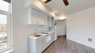 Located at 2180 NE 47th Ave in Portland, Oregon, this single-floor studio unit offers a thoughtfully designed open-plan layout that combines the living, dining, and kitchen areas into one cohesive space. The entrance opens into a clean, neutral-toned corridor finished with wood-look luxury vinyl plank flooring that carries throughout the unit, lending a sense of continuity and warmth.

The kitchen is a standout feature, outfitted with sleek gray flat-front cabinetry, white quartz countertops, a stainless steel undermount sink with a modern gooseneck faucet, an electric cooktop, a built-in microwave, a dishwasher, and a full-size refrigerator. Upper cabinets and open shelving provide ample storage, while a large window allows natural light to brighten the workspace. A range hood and recessed lighting contribute to the practical, well-lit environment.

The main living area is open and versatile, featuring crisp white walls and a ceiling fan, creating a comfortable and adaptable environment. A closet rod offers built-in storage within the living space.

The bathroom is clean and functional, finished with the same vinyl plank flooring and equipped with a grab bar, toilet, and shower area. The bright white walls and simple fixtures maintain the unit's modern, minimal aesthetic throughout.