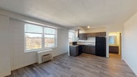 Located at 2515 Burnet Ave in Cincinnati's vibrant Corryville neighborhood, this single-floor unit offers a well-organized and efficiently designed living space. The open-concept layout seamlessly connects the living area to the kitchen, creating a spacious and airy feel throughout. Large windows flood the main living area with generous natural light while framing pleasant outdoor views of the surrounding landscape, enhancing the sense of openness. A wall-mounted HVAC unit provides climate control directly in the living space.

The kitchen is outfitted with dark espresso cabinetry, granite-style countertops, and black appliances including a range, overhead hood vent, and full-size refrigerator. A stainless steel sink and additional upper and lower cabinet storage complete this functional cooking area.

The living space features light-toned wood-style flooring that runs consistently throughout, adding warmth and visual continuity. White painted walls and a textured ceiling contribute to a clean, neutral aesthetic throughout the unit.

The bathroom is neatly appointed with a combined tub and shower, a toilet, and matching wood-style flooring, maintaining the cohesive design language of the rest of the unit. The space is practical, well-lit, and move-in ready.