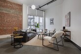 Located at 620 S Main St in the heart of Downtown Los Angeles, this single-floor industrial loft showcases a striking blend of raw architectural character and contemporary design. Soaring ceilings amplify the sense of openness throughout, while polished concrete floors run continuously across the space, lending a refined yet urban aesthetic.

The expansive main living area is anchored by large windows that invite natural light and offer views of the surrounding cityscape. Track lighting and globe pendant fixtures complement the industrial framework of exposed pipes and structural columns. Original exposed brick walls and concrete columns add authentic character to multiple zones within the loft.

The living spaces are thoughtfully arranged with distinct seating areas, each featuring curated furnishings and original artwork. A galley-style kitchen is outfitted with dark cabinetry, white quartz countertops, stainless steel appliances, a gas range, and in-unit laundry — combining practicality with sleek design.

The sleeping area is defined by a folding screen partition, maintaining an open-plan feel while offering privacy. The bathroom features a classic black-and-white tiled shower-tub combination with polished concrete flooring continuing from the main space. Throughout, the loft presents a cohesive industrial-modern atmosphere suited for urban living in Downtown Los Angeles.