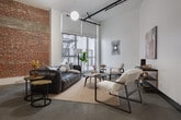 Located at 620 S Main St in the heart of Downtown Los Angeles, this single-floor industrial loft showcases a striking blend of raw architectural character and contemporary design. Soaring ceilings amplify the sense of openness throughout, while polished concrete floors run continuously across the space, lending a refined yet urban aesthetic.

The expansive main living area is anchored by large windows that invite natural light and offer views of the surrounding cityscape. Track lighting and globe pendant fixtures complement the industrial framework of exposed pipes and structural columns. Original exposed brick walls and concrete columns add authentic character to multiple zones within the loft.

The living spaces are thoughtfully arranged with distinct seating areas, each featuring curated furnishings and original artwork. A galley-style kitchen is outfitted with dark cabinetry, white quartz countertops, stainless steel appliances, a gas range, and in-unit laundry — combining practicality with sleek design.

The sleeping area is defined by a folding screen partition, maintaining an open-plan feel while offering privacy. The bathroom features a classic black-and-white tiled shower-tub combination with polished concrete flooring continuing from the main space. Throughout, the loft presents a cohesive industrial-modern atmosphere suited for urban living in Downtown Los Angeles.