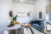 This efficiently designed studio in Jonesboro, Arkansas makes a strong impression with its dramatic soaring ceilings and polished concrete floors that run throughout the open-plan living space. The living area is bright and airy, offering ample room for a full seating arrangement, with clean white walls that amplify the sense of openness and height.

The kitchen is sleekly outfitted with light wood cabinetry, quartz-style countertops, a stainless steel refrigerator, electric range, and an over-the-range microwave — all designed for both function and style. A stainless steel sink completes the practical workspace.

The sleeping area is tucked away with a sense of privacy and features a generous reach-in closet with sliding wood-panel doors. Soaring walls continue into this space, reinforcing the open, loft-like character of the unit.

The full bathroom is well-utilized, housing a shower/tub combination with a striped curtain, a pedestal-style sink, and a stacked Whirlpool washer and dryer unit — a notable convenience built directly into the space. Natural wood-toned doors appear throughout, adding warmth against the predominantly white and neutral palette. The overall ambiance is modern, clean, and thoughtfully designed to maximize every square foot.