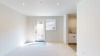 This well-designed single-floor unit offers a clean, modern aesthetic throughout, characterized by bright white walls, recessed lighting, and neutral carpet flooring that flows seamlessly across the main living areas. The open-concept layout connects the kitchen and living space, creating a generous, functional area ideal for everyday living.

The kitchen is thoughtfully appointed with white shaker-style cabinetry accented by matte black hardware, a classic subway tile backsplash, light quartz countertops, and a suite of stainless steel appliances including a gas range, over-the-range microwave, and refrigerator. A utility sink adds further practicality to the space.

The expansive living area benefits from natural light through a glass-paneled exterior door and an adjacent window, lending the space an airy, open feel. A private exterior entrance provides convenient and direct access.

The bathroom is finished in a crisp, minimalist style, featuring white subway tile surrounding a soaking tub and shower combination, a marble-topped vanity, and matte black fixtures and accessories. Polished concrete flooring completes the clean look.

A dedicated laundry room with in-unit washer, utility sink, and an electrical panel offers exceptional functionality. The unit also includes a spacious walk-in closet, providing ample storage. The overall design is fresh, neutral, and move-in ready.