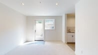 This well-designed single-floor unit offers a clean, modern aesthetic throughout, characterized by bright white walls, recessed lighting, and neutral carpet flooring that flows seamlessly across the main living areas. The open-concept layout connects the kitchen and living space, creating a generous, functional area ideal for everyday living.

The kitchen is thoughtfully appointed with white shaker-style cabinetry accented by matte black hardware, a classic subway tile backsplash, light quartz countertops, and a suite of stainless steel appliances including a gas range, over-the-range microwave, and refrigerator. A utility sink adds further practicality to the space.

The expansive living area benefits from natural light through a glass-paneled exterior door and an adjacent window, lending the space an airy, open feel. A private exterior entrance provides convenient and direct access.

The bathroom is finished in a crisp, minimalist style, featuring white subway tile surrounding a soaking tub and shower combination, a marble-topped vanity, and matte black fixtures and accessories. Polished concrete flooring completes the clean look.

A dedicated laundry room with in-unit washer, utility sink, and an electrical panel offers exceptional functionality. The unit also includes a spacious walk-in closet, providing ample storage. The overall design is fresh, neutral, and move-in ready.