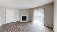 Located at 18175 Midway Rd in Dallas, TX, this single-floor unit offers a functional and well-appointed layout throughout. Rich, dark wood-look flooring runs consistently across all living areas, creating a cohesive and modern aesthetic.

The living room is a welcoming, open space anchored by a classic white-surround fireplace and a large sliding glass door fitted with vertical blinds, allowing ample natural light to fill the room while providing access to the outdoors. Adjacent to the living area is a dedicated dining space that connects seamlessly to the kitchen.

The kitchen features a galley-style layout with white cabinetry, light stone-pattern countertops, and a full suite of black appliances including a range, microwave, refrigerator, and dishwasher. A stainless steel double sink completes the workspace.

The bedroom is generously sized with a natural light source from a window and includes a walk-in closet with built-in shelving and a hanging rod, offering excellent storage capacity. Textured popcorn ceilings are present throughout the unit.

The bathroom is clean and straightforward, featuring a full soaking tub with an overhead shower, white tile surround, and standard fixtures. The overall ambiance of the space is neutral and move-in ready, with a palette of warm grays and whites throughout.