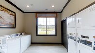 Located at 45 Lullwater Dr in Richmond Hill, Georgia, this single-floor laundry facility is designed for convenience and functionality. The room is finished with neutral-toned walls, dark contrasting trim, and light-colored flooring, giving the space a clean and well-maintained appearance. Recessed lighting in the ceiling provides consistent illumination throughout the room, complemented by a large window framed with a decorative wooden valance. The window allows ample natural light to fill the space and offers an open view of the green outdoor surroundings, creating a pleasant environment. The facility is equipped with both top-loading and stacked washer-dryer units, offering flexible laundry options to accommodate various needs. A dark-painted door provides access to an adjacent area, contributing to the overall flow of the space. The combination of practical amenities, thoughtful design details, and a bright, airy atmosphere makes this laundry facility a well-appointed and user-friendly space.