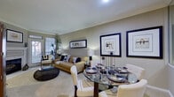 This thoughtfully designed single-floor residence offers a cohesive and comfortable living environment with a warm, neutral color palette throughout. The open-concept living and dining area serves as the heart of the home, featuring crown molding, plush carpeted flooring, and a cozy fireplace. Natural light filters in through large windows, illuminating the space and highlighting framed wall art that adds a refined touch. A glass-top dining table with upholstered chairs sits adjacent to the living area, creating a seamless transition between spaces.

The kitchen is efficiently laid out with warm wood cabinetry, white appliances including a range, microwave, and refrigerator, and ample counter and storage space. Clean white tile flooring and recessed lighting give the kitchen a bright, functional feel.

The bedroom is a serene retreat, featuring large windows that invite natural light and offer views of greenery outside. Crown molding, soft carpet, a ceiling fan, and well-chosen furnishings contribute to a restful atmosphere.

The bathroom is clean and modern, finished with white tile flooring, a wide vanity with an extended mirror, recessed lighting, and a glass-enclosed shower, providing a polished and practical space.