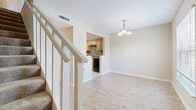 Located at 541 Oak Reserve Lane in Winter Park, Florida, this two-story home offers a practical and comfortable layout spread across two floors. The main level features a bright living room with light wood-style flooring, a chandelier pendant light, and a door leading to an outdoor area, allowing natural light to flow in alongside views of surrounding greenery. Adjacent to the living room, the kitchen is accessible via a pass-through opening and is equipped with light wood cabinetry, dark countertops, a mosaic tile backsplash, tile flooring, and black appliances including a range and dishwasher. A carpeted staircase with a white wood banister connects the two floors.

Upstairs, both bedrooms are finished with plush carpet and feature windows that bring in natural light and outdoor views. The primary bedroom is generously sized and includes two closets — a double-door closet and an additional single door closet — providing ample storage. The second bedroom also offers comfortable proportions with a bright window outlook. Each floor is served by its own bathroom; the bathrooms feature tile flooring, warm wood vanities with light countertops, and textured walls. Hallways on both levels provide smooth circulation throughout the home.