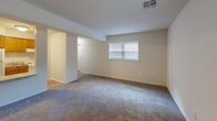 Located at 39 Abbey Ln in Newark, Delaware, this single-floor unit offers a practical and efficient layout comprising a living room, kitchen, and full bathroom. The living room is generously proportioned for the overall footprint of the space, featuring wall-to-wall carpeting in a neutral gray tone and multiple windows that allow natural light to filter in, creating a bright and open atmosphere. The walls are painted in a clean, soft beige, contributing to the unit's simple, understated aesthetic. A central ceiling vent provides climate control throughout. The kitchen is thoughtfully arranged, featuring warm-toned wood cabinetry with ample upper and lower storage, a granite-style countertop, a stainless steel sink, and a full-size white refrigerator. The flooring in the kitchen transitions to wood-look vinyl planking, offering both durability and visual contrast to the carpeted living area. The bathroom includes a classic tub and shower combination with white square tile surround and a warm-toned tub, complemented by chrome fixtures. The overall layout, as seen in the dollhouse view, is compact yet well-organized, with clearly defined zones for living, cooking, and bathing — making efficient use of the available space.