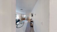 This thoughtfully laid-out single-floor residence offers a comfortable and functional living experience across six distinct spaces. The open-concept living room is bathed in natural light and features warm wood-look flooring, crisp white walls, and a textured ceiling. A wall-mounted TV, stylish lean-to bookshelf, and a seating arrangement centered around a glass coffee table give the space a modern, welcoming character.

Adjacent to the living room, the dedicated dining area accommodates a round four-seat table and benefits from a large window with vertical blinds that allow for adjustable natural light. The kitchen is outfitted with white shaker-style cabinetry, light tile flooring, and stainless steel appliances including a dishwasher and full-size refrigerator, providing ample prep and storage space.

The bedroom is a calm retreat with wood-look flooring, a ceiling fan, and a window dressed with wooden blinds that filters soft natural light. A dedicated closet adds practical storage. The bathroom features a full tub-shower combination with white tile surround, maintaining the clean, neutral aesthetic found throughout the residence. Overall, the space presents a bright, cohesive design with consistent finishes that create a polished and livable environment.