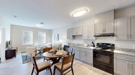 This well-designed one-bedroom, two-bathroom residence makes efficient use of its single-floor layout, offering a cohesive open-plan living space that integrates the kitchen, dining, and living areas seamlessly. Light wood-style flooring runs throughout the main living areas, complementing the neutral warm-gray and beige color palette that creates a bright, cohesive aesthetic.

The kitchen is outfitted with gray shaker-style cabinetry, granite-look countertops, and black appliances including a range, dishwasher, and full-size refrigerator. A round dining table sits conveniently adjacent to the kitchen, providing a defined dining area within the open layout. The living room receives natural light through multiple windows fitted with blinds and offers comfortable space for seating arrangements.

The primary bedroom features carpeted flooring, two windows, and a reach-in closet with built-in shelving, providing practical storage. The neutral tones carry through to this room, maintaining a calm and restful atmosphere.

Two bathrooms serve the unit, one featuring a full tub-shower combination with white tile surround. Flush-mount lighting is used consistently throughout, and the entry area includes a closet, adding to the unit's overall storage capacity.
