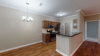 This single-floor residence at 8913 Old Bardstown Rd in Louisville, Kentucky, offers a well-designed layout with a cohesive blend of practical features and inviting finishes. The open-concept kitchen is a central highlight, equipped with stainless steel appliances including a refrigerator, electric range, and over-the-range microwave. Rich wood-toned cabinetry provides ample storage, while a peninsula with a dark countertop creates a natural divide between the kitchen and the adjoining dining area. The dining space is accentuated by a classic chandelier and warm hardwood-style flooring that extends throughout the main living areas. Crown molding is present throughout, adding a refined architectural detail to each room. The spacious living room features a ceiling fan with light fixture and a sliding glass door dressed with vertical blinds, inviting natural light. Bedrooms are carpeted for comfort, with ceiling fans and windows that bring in additional daylight. The bathrooms include a full bath with a wide double-sink vanity, generous mirror, and a separate water closet, as well as a convenient half bath with a wood-cabinet vanity. The overall palette of neutral warm tones and clean white trim creates a bright, welcoming ambiance throughout the home.