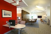 Located at 3857 Flowerfield Rd in Norfolk, Virginia, this single-floor community clubhouse offers a thoughtfully designed gathering space that blends comfort, functionality, and character. The main lounge area serves as the heart of the facility, featuring plush neutral armchairs, patterned carpeting in soft blue-gray tones, and bold orange accent walls that add a vibrant, energetic contrast to the otherwise airy interior. A striking sputnik-style chandelier anchors the ceiling, while tall windows flood the space with abundant natural light and provide clear views of the outdoor pool area.

A standout feature is the floor-to-ceiling brick fireplace framed by comfortable seating, creating an inviting focal point ideal for relaxed gatherings. Adjacent to the lounge, a dramatic patriotic mural wall — depicting vintage American flags in warm, distressed tones — acts as a bold architectural divider between the lounge and dining areas.

The dining area offers a mix of booth-style banquette seating and freestanding tables with mixed wooden and woven chairs, complemented by pendant lighting and a wall-mounted display screen. Large windows here also overlook the pool courtyard. A fully equipped kitchen with stainless steel appliances, ample cabinetry, and a pass-through window supports event hosting and everyday community use. Together, these spaces create a cohesive, welcoming environment for residents.