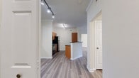 This 850-square-foot, single-floor apartment at The Colonnade (4100 Central Pike, Hermitage, TN) features 2 bedrooms and 2 bathrooms with consistent hardwood-style flooring throughout. The open-concept kitchen and living area is anchored by a breakfast bar with dark granite countertops, warm wood cabinetry, and black appliances. Crown molding and track lighting add a polished touch to the space. The living room is a standout, featuring a stacked-stone fireplace with a white mantel and a glass door leading to an outdoor patio, allowing abundant natural light. Both bedrooms include ceiling fans and windows with outdoor views; the primary bedroom measures 150 square feet and offers dual closets, while a separate walk-in closet features a built-in wood shelving and drawer system. The primary bathroom includes a soaking tub with tile surround, a wide vanity with ample cabinetry, and a large mirror. The second bathroom features a tiled shower and matching wood vanity. A dedicated laundry room houses a full-size washer and dryer. The unit is completed by a hallway connecting all rooms efficiently, making for a practical and comfortable layout.