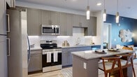 This 2-bedroom, 2-bathroom residence is designed with a modern aesthetic and practical open-concept layout. The combined kitchen and living area serves as the heart of the home, featuring a sleek kitchen outfitted with gray shaker-style cabinetry, granite countertops, stainless steel appliances, a white hexagonal tile backsplash, and a central island with pendant lighting — ideal for both cooking and casual dining. The living area flows naturally from the kitchen, highlighted by floor-to-ceiling French doors that invite natural light and feature a bold navy accent wall. Each bedroom offers a comfortable, carpeted retreat with ceiling fans and natural light from well-positioned windows. The spacious primary bedroom provides a generous footprint, while the second bedroom is equally inviting with bright windows and tasteful finishes. Both bathrooms echo the kitchen's design language, featuring gray vanity cabinetry, granite countertops, hardwood-style flooring, and tub-shower combinations with marble-style tile surrounds. Additional conveniences include two closets, a dedicated laundry area, and a utility room, rounding out this efficiently designed and stylishly finished residence.