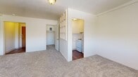 Located at 130 S 500 E in Salt Lake City, Utah, this one-bedroom, one-bathroom unit offers a well-organized layout across a single floor. The entrance opens into the main living area, which is generously sized relative to the overall footprint and features soft carpet flooring, light neutral walls, and a wide window fitted with horizontal blinds that allows natural light to fill the room. A wall-unit heater sits beneath the window, providing in-unit climate control. A distinctive open lattice-style partition wall separates the living area from the kitchen nook, adding a subtle architectural detail while maintaining visual openness. The kitchen is equipped with white cabinetry, a white electric range, and durable hardwood-style flooring, offering a clean and functional cooking space. A dedicated closet provides built-in storage off the main living area. The spacious bedroom is carpeted and benefits from its own window with natural light and outdoor views. The bathroom features hardwood-style flooring, a full-size soaking tub with shower, and clean white finishes throughout. The overall aesthetic is clean and understated, presenting a practical and comfortable living space in a convenient Salt Lake City location.