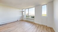 Located on the 10th floor at 70 Spadina Rd in Toronto's sought-after Annex neighbourhood, this efficiently laid-out unit offers a clean, modern aesthetic throughout. The space is finished with light-toned hardwood-style flooring that runs continuously, complementing the crisp white walls and creating a bright, airy atmosphere.

The two living areas are generously lit by large floor-to-ceiling windows that frame expansive views of the surrounding treetops, residential rooftops, and the Toronto skyline in the distance. A private balcony is accessible from the main living area, extending the sense of openness. Built-in baseboard heaters line the windows, and one of the living areas features a full-height mirrored sliding closet, adding both storage and a reflective depth to the room.

The bathroom is neatly appointed with classic white subway tile surrounding a soaking tub and shower combination, a compact vanity with a white finish, tile flooring, and chrome fixtures — delivering a clean and functional design.

Throughout the unit, the minimalist white palette, abundant natural light, and elevated treetop and city views combine to create a calm, comfortable living environment in one of Toronto's most vibrant and walkable neighbourhoods.