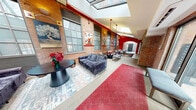 Located at 30 Laurel St in Hartford, Connecticut, this distinctive lobby and common area seamlessly merges industrial history with contemporary design. The single-floor layout encompasses a generously sized living/lounge area and two connecting hallways, all unified by a cohesive aesthetic that celebrates the building's original character.

Exposed brick walls run throughout the space, serving as a warm, textured backdrop for a rotating gallery of vibrant, large-format artworks. Soaring ceilings with skylights flood the interior with natural light, while bold red architectural elements — including painted columns, beams, and accent piping — inject energy and a distinct visual identity. Light-toned tile flooring contrasts with a rich red runner carpet that guides visitors through the elongated corridor.

The lounge area is thoughtfully furnished with plush grey sofas, modern accent chairs, and sleek coffee tables, creating inviting seating clusters suited for relaxation or casual gathering. An elevator provides building access, and arched brick doorways nod to the structure's historic roots. Industrial-style steel windows add to the authentic loft character, while carefully placed lighting and curated floral arrangements contribute warmth and polish. The result is a welcoming, art-forward communal space that honors Hartford's architectural heritage.