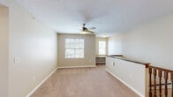 This single-floor residential unit offers a functional and comfortable layout designed to maximize livable space. The open-concept living and dining area is finished with warm beige carpet and neutral-toned walls, creating a bright and welcoming atmosphere. A ceiling fan with integrated lighting serves as a central fixture, while multiple windows allow natural light to flow freely throughout the space and offer views of the surrounding neighborhood.

The kitchen is efficiently designed with rich dark-stained cabinetry, granite-patterned countertops, and a full suite of black appliances including a refrigerator, range, and built-in microwave. Light wood-style flooring runs through the kitchen, complementing the cabinetry tones. A peninsula counter separates the kitchen from the living area, providing additional prep space and a natural transition between the two zones.

The bedrooms are carpeted and finished with the same neutral palette, offering a calm and restful environment. Each room includes windows that bring in natural light. A full bathroom features dark wood cabinetry, a combination tub and shower, wood-style flooring, and a single-sink vanity. A staircase with a classic wood banister provides access between levels, adding a traditional architectural touch to the overall design.
