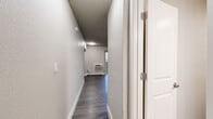 Located at 1810 Monterey Rd in Colorado Springs, CO, this efficiently designed single-floor unit makes smart use of its compact footprint. The main living area features durable wood-style laminate flooring in a cool gray tone, neutral light gray walls, and a textured ceiling. A wall-mounted HVAC unit and a baseboard heater provide year-round climate control, while vertical blinds on a sliding or full-length window allow for natural light and ventilation.

An open closet with a clothing rod is built directly into the living area wall, offering convenient storage without sacrificing floor space. A narrow hallway connects the living area to the kitchen and bathroom, maintaining a clear and functional layout.

The kitchen is well-appointed with crisp white shaker-style cabinetry, granite-look countertops, a stainless steel sink, black appliances including a refrigerator and electric range with overhead ventilation, and continued wood-style flooring. Flush ceiling lighting keeps the space bright and practical.

The bathroom features the same wood-style flooring, a full bathtub with an overhead shower, a toilet, and towel bars with brushed nickel hardware. Clean white walls and minimalist fixtures give the bathroom a tidy, functional character. Overall, the unit presents a clean, updated aesthetic suitable for efficient, comfortable living.