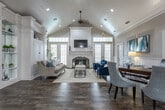 Located in Gainesville, Georgia, this single-story community space combines classic Southern architecture with refined coastal-inspired design. The welcoming entryway greets visitors with rich hardwood flooring, white decorative columns, crown molding, and a striking pendant chandelier that sets the tone for the interior. Large glass-paneled front doors with sidelights flood the foyer with natural light, while navy blue drapery adds a bold, polished accent.

The main living area is a standout, featuring soaring vaulted ceilings finished with white beadboard paneling and recessed lighting. A central fireplace with an elegant white surround and dark stone hearth serves as the focal point of the room, complemented by a wall-mounted television above the mantle. Comfortable seating, including a neutral linen sofa and deep navy accent chairs, creates an inviting gathering space framed by multiple French doors and windows.

A private office area offers a professional setting with a classic wood desk, upholstered guest chairs, and glass-paned interior doors that maintain an open, airy feel while providing privacy. Throughout the space, consistent use of white wainscoting, soft gray walls, and dark hardwood floors creates a cohesive, sophisticated aesthetic. The overall ambiance is bright, elegant, and welcoming.