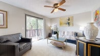 This well-appointed single-floor residence in Wichita, Kansas offers a thoughtfully designed layout that maximizes comfort and functionality. The living room serves as the heart of the home, featuring plush carpeting, a ceiling fan, and a large sliding glass door that opens onto a private balcony overlooking lush, mature trees — filling the space with abundant natural light and serene outdoor views. The kitchen is efficiently designed with dark cabinetry, light countertops, and a pass-through peninsula that connects seamlessly to the dining area. The dining space accommodates a glass-top table and provides an open, airy feel enhanced by a chandelier overhead. A spacious hallway connects the main living areas to the private quarters, offering additional room for furnishings or decorative accents. The bedroom is generously sized, featuring soft carpeting, a ceiling fan, and a window that allows natural light to filter in. It includes access to a walk-in closet and is conveniently positioned near the bathroom, which features a clean, full-sized soaking tub and shower combination. Throughout the residence, textured ceilings, neutral tones, and carpeted floors create a cohesive and inviting ambiance suited for comfortable everyday living.