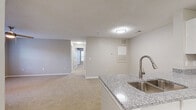 This single-floor residence offers a thoughtfully designed layout that balances open communal spaces with comfortable private quarters. The kitchen serves as a central highlight, featuring crisp white cabinetry, granite-look countertops, black appliances including an electric range, and wood-look flooring that adds warmth and durability. A peninsula with a stainless steel sink connects the kitchen to the open living area, which is finished with plush carpeting and a ceiling fan. A sliding glass door in the living room provides direct access to a private outdoor space, filling the room with natural light. Multiple bedrooms carry a consistent aesthetic with neutral-toned walls, soft carpeting, and windows fitted with blinds. The primary bedroom is well-sized and benefits from natural light and ceiling fan comfort. Two bathrooms continue the refined finishes seen throughout, each featuring granite-look countertops and white cabinetry. One includes a tub-shower combination with white tile surround, while the other mirrors the same clean design. A hallway connects the private rooms, creating a clear and functional separation between living and sleeping areas. The overall palette of warm neutrals and clean white trim gives the space a move-in-ready, cohesive feel.