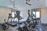 Located in Atlanta, GA, this single-floor fitness center at Parkwood Circle SE offers a well-equipped workout facility designed to support a wide range of exercise routines. The space is thoughtfully laid out across several connected areas, each serving a distinct fitness purpose.

The cardio zone features a row of Matrix treadmills positioned in front of large windows that invite natural light and provide views of the surrounding greenery — an energizing backdrop for any workout session. Recessed lighting and a ceiling fan overhead contribute to a comfortable environment during high-intensity training.

Adjacent to the cardio area, a dedicated strength training section houses a Matrix functional trainer cable machine paired with a weight bench, offering versatile resistance training options. This area also benefits from generous window exposure, keeping the space bright and well-ventilated.

A striking curved teal accent wall anchors the central zone of the facility, creating a bold visual focal point while also housing additional Matrix cardio equipment, including a stationary bike and a rowing machine. The rubber flooring throughout provides durability and safety underfoot.

A separate studio or multipurpose room features warm hardwood-style flooring, a ceiling fan, recessed lighting, and large interior glass windows that maintain an open visual connection to the main gym floor — ideal for group fitness classes or individual stretching and yoga sessions.