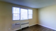 Located at 118 Montgomery Avenue in Bala Cynwyd, Pennsylvania, this single-floor unit offers a straightforward and functional layout designed for comfortable everyday living. The space features rich, dark hardwood flooring that extends throughout, providing a warm and grounded aesthetic that contrasts pleasantly with the soft, neutral yellow-toned walls.

Natural light is a defining characteristic of the space, with a large multi-pane window prominently positioned to draw in abundant daylight and offer views of the surrounding neighborhood's mature trees and streetscape. Horizontal blinds provide flexible light control. The textured ceiling adds a subtle visual layer to the interior.

Climate comfort is well-addressed, with both a wall-mounted air conditioning unit and a baseboard radiator present beneath the main window, ensuring year-round temperature management. Clean white baseboards frame the perimeter of the room, contributing to a tidy, well-maintained appearance.

The overall ambiance of the space is bright, clean, and move-in ready, with a simple yet inviting character. Situated in the desirable Bala Cynwyd area of Lower Merion Township, the location offers convenient access to local amenities, transit options, and the broader Philadelphia metropolitan region.