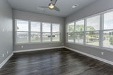 This single-floor residence presents a cohesive modern design with consistent finishes carried throughout each room. The kitchen serves as a functional centerpiece, outfitted with dark espresso cabinetry, granite countertops, a subway tile backsplash, and a full suite of stainless steel appliances including a refrigerator, electric range, and built-in microwave. Glass-front upper cabinets add a refined detail, while a granite-topped island provides additional prep and seating space beneath pendant lighting. Wood-look plank flooring runs through the kitchen, living, and dining areas, lending warmth and continuity.

The living area is generously proportioned, featuring large windows with exterior views, a ceiling fan, and direct access to an outdoor balcony. Additional rooms used as bedrooms are carpeted and receive natural light through windows overlooking green outdoor scenery.

Both bathrooms are finished with dark cabinetry, granite countertops, and wood-look flooring. The primary bathroom includes a dual-sink vanity and a glass-enclosed shower, while the secondary bathroom features a full soaking tub with tiled surround. The layout, as seen in the dollhouse overview, is well-organized with clear separation between living and private spaces.