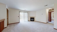 Located at 21900 Foxhaven Run in Waukesha, Wisconsin, this one-bedroom, one-bathroom home offers a well-organized, single-floor layout with a comfortable and functional design throughout. The living room serves as the heart of the home, featuring a tile-surround fireplace with a clean white mantle as a focal point, plush neutral carpeting, and a large sliding glass door fitted with vertical blinds that floods the space with natural light and provides outdoor views. The kitchen is efficiently designed with ample white cabinetry accented by warm wood trim, a peninsula counter that opens toward the living area, light tile flooring, and a full suite of black appliances including a refrigerator, range, dishwasher, and over-range microwave. The bedroom is a well-proportioned, quiet retreat with soft carpeting, neutral walls, and a wood-trimmed window that brings in natural light. The bathroom is clean and straightforward, featuring a full soaking tub with shower, tile flooring, and accessible grab bars. Warm wood baseboards and trim are consistent throughout, lending a cohesive and classic aesthetic to the entire home.