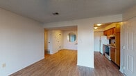 This single-floor residence is thoughtfully laid out to maximize functionality across its living spaces. The open living and dining area features light wood-tone laminate flooring and a ceiling fan with integrated lighting, creating a bright and airy atmosphere. A distinctive circular mirror accent on the partial dividing wall adds a unique architectural touch, while easy sightlines connect the living space to both the entryway and kitchen.

The galley-style kitchen is well-appointed with warm wood cabinetry lining both walls, offering generous storage and counter space. It is equipped with a double-basin sink, electric range, dishwasher, and refrigerator, all set over matching laminate flooring that flows seamlessly from the main living area.

The bedrooms are carpeted for comfort and each includes a ceiling fan. One bedroom features a walk-in closet with shelving, providing ample storage. Each room offers a quiet, neutral palette suitable for a variety of furnishing styles.

The full bathroom is clean and functional, featuring a tub and shower combination, a vanity with a single sink and storage cabinetry below, and a large wall mirror. Textured ceilings are consistent throughout the unit, contributing to the home's classic residential character. The layout is efficient and well-connected, making this a practical and comfortable living space.