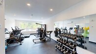 Located at 200 Garden St in South Burlington, Vermont, this fitness center offers a comprehensive workout facility within a compact, single-floor layout. The space is designed with functionality and cleanliness in mind, featuring crisp white walls, recessed lighting, and a durable dark concrete floor that gives the room a modern, professional feel.

The exercise room is thoughtfully organized to maximize utility. A full-length mirror wall spans one side of the room, visually expanding the space and providing workout feedback. Large windows along one wall allow natural light to fill the room while offering views of the surrounding greenery outside.

Cardio equipment includes multiple True-brand treadmills, an elliptical trainer, and a stationary spin bike, all positioned to take advantage of the natural light. A multi-station cable and weight machine anchors the strength training area, complemented by a tiered dumbbell rack stocked with a comprehensive range of free weights and an adjustable workout bench. A dedicated accessories station houses stability balls, resistance bands, yoga mats, and medicine balls, supporting a full range of training modalities.

Climate comfort is maintained by a wall-mounted mini-split HVAC unit. With its well-rounded equipment selection and clean, organized design, this fitness center provides residents with everything needed for a complete and effective workout routine.