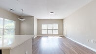 Located at 7815 Calibre Crossing Dr in Matthews, NC, this single-story unit offers a well-designed open-concept layout finished with warm wood-style flooring that extends throughout the living areas. The spacious living and dining area is flooded with natural light from multiple windows dressed with horizontal blinds, creating a bright and welcoming atmosphere. Neutral taupe-toned walls complement the clean white trim and baseboards, lending a cohesive, move-in-ready aesthetic.

The kitchen is positioned centrally within the open floor plan and features white cabinetry, light-toned countertops, a classic tile backsplash, and stainless steel appliances including a refrigerator, range, and microwave. A peninsula with an integrated sink provides both additional prep space and a natural divider between the kitchen and living areas, with a pendant light overhead adding a refined touch.

The bedroom offers generous proportions, wood-style flooring, and a large window that brings in natural light and views of the surroundings. The bathroom includes a soaking tub and shower combination with white tile surround. A dedicated laundry area accommodates a full-size washer and dryer with overhead shelving for storage. Overall, the space presents a clean, functional, and comfortable living environment.